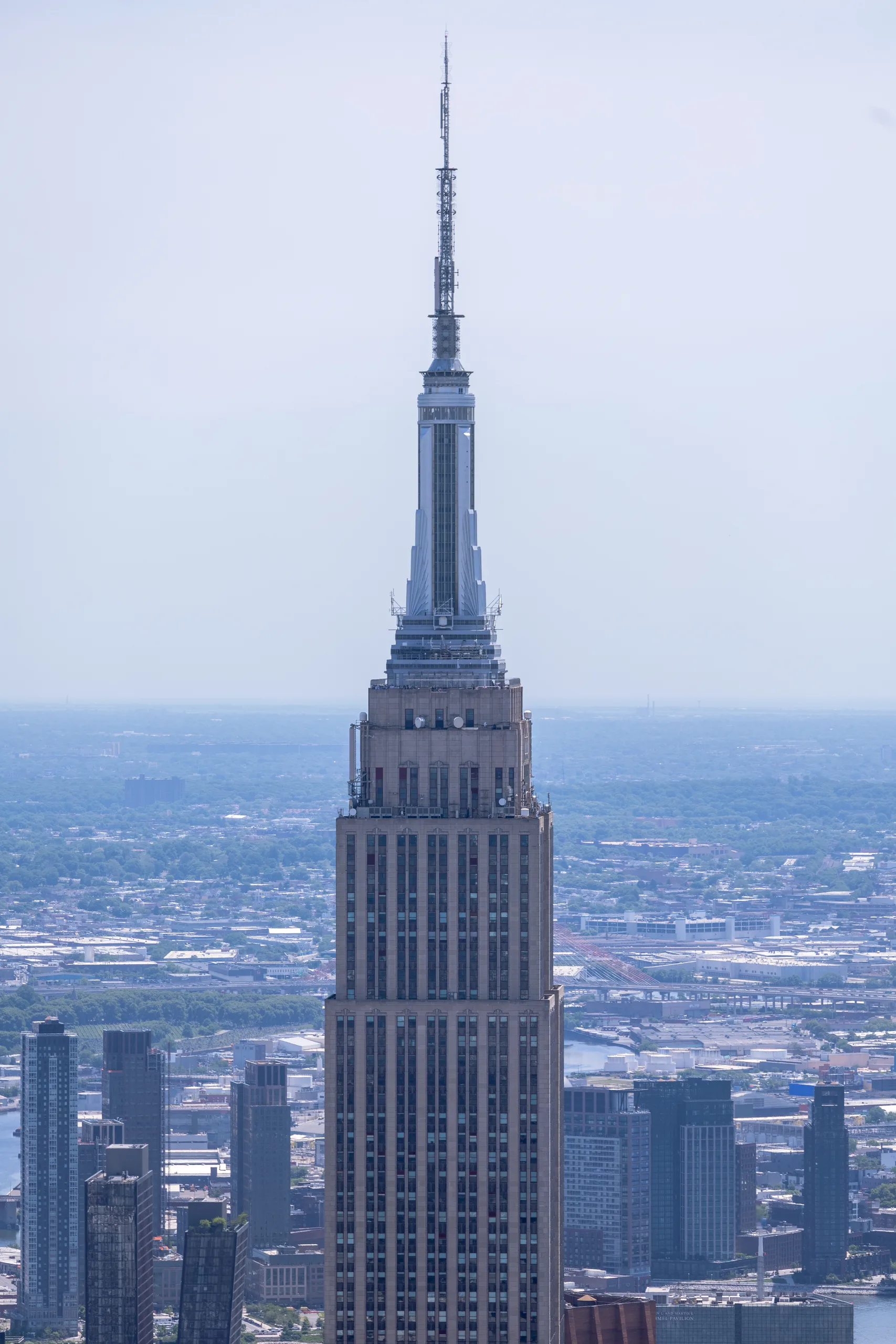 The upper setbacks and mast of the Empire State Building above the Manhattan skyline, with the harbour behind it.